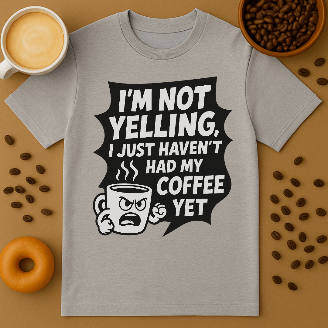 Gray t-shirt with coffee-themed graphic and text on a brown background with coffee beans and a donut.