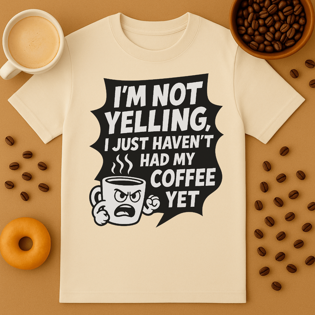 Beige t-shirt with coffee-themed graphic and text on a brown background with coffee beans and a donut.